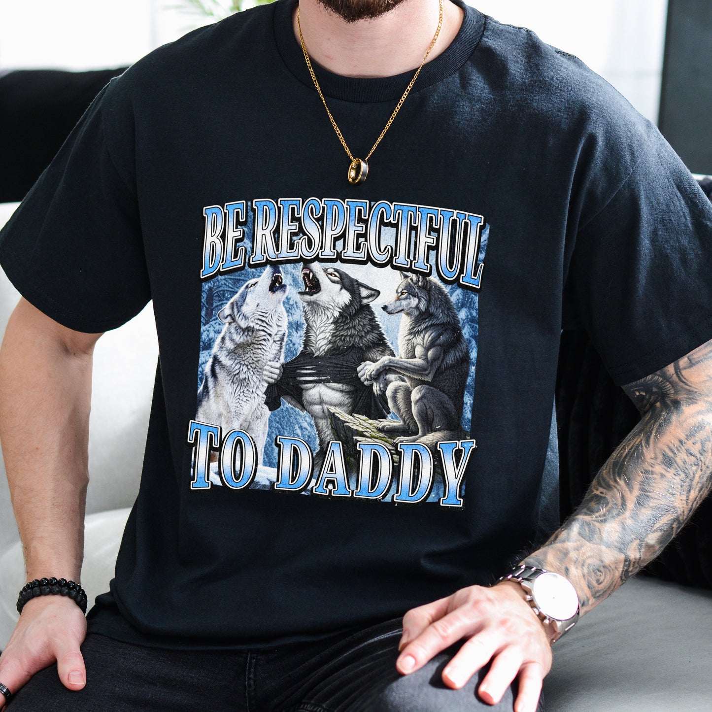 Person wearing a black t-shirt with a graphic design and text, sitting on a couch.