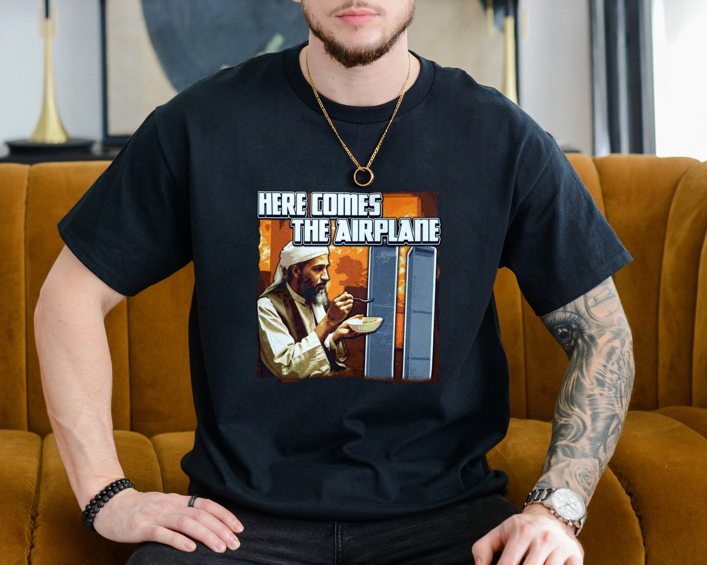 Person wearing a black t-shirt with a graphic design sitting on a mustard yellow couch.