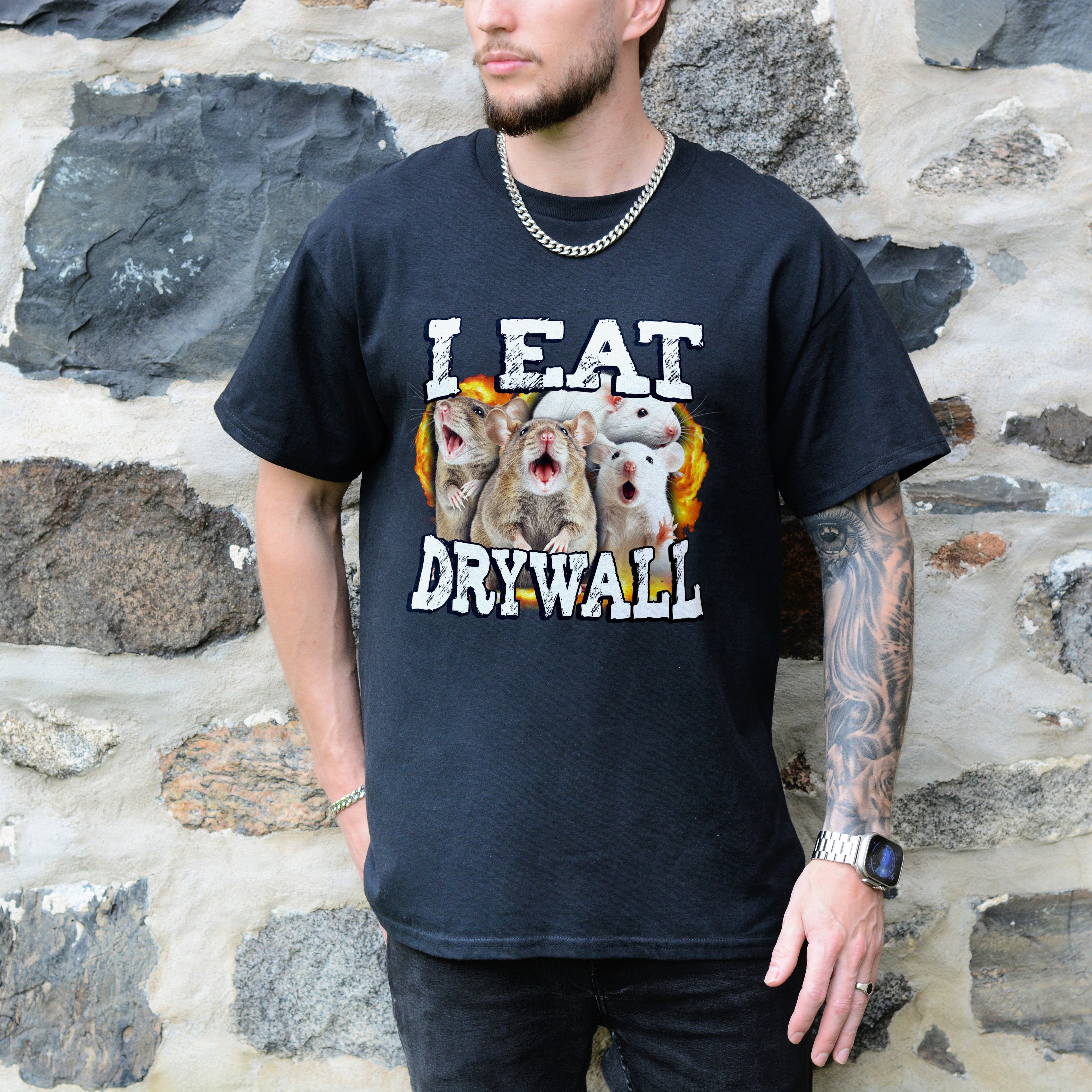 Person wearing a black t-shirt with a graphic design and text, standing against a stone wall.