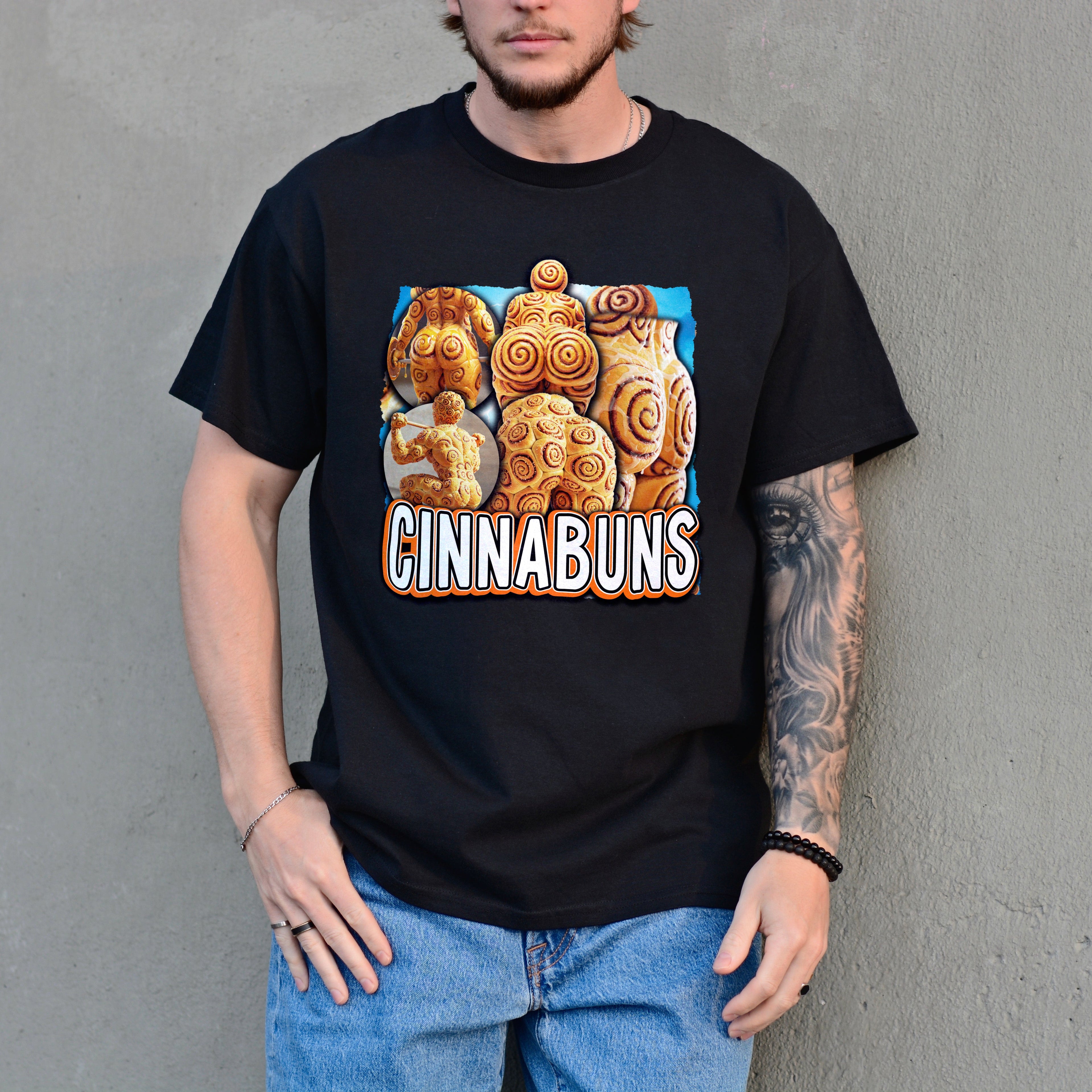 Person wearing a black t-shirt with a 'Cinnabuns' graphic design against a gray wall.