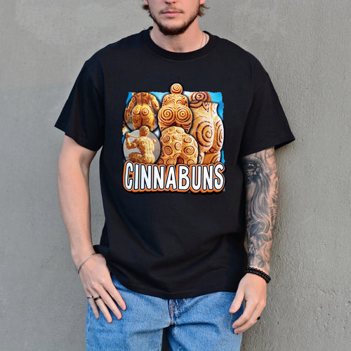 Person wearing a black t-shirt with a 'Cinnabuns' graphic design against a gray wall.