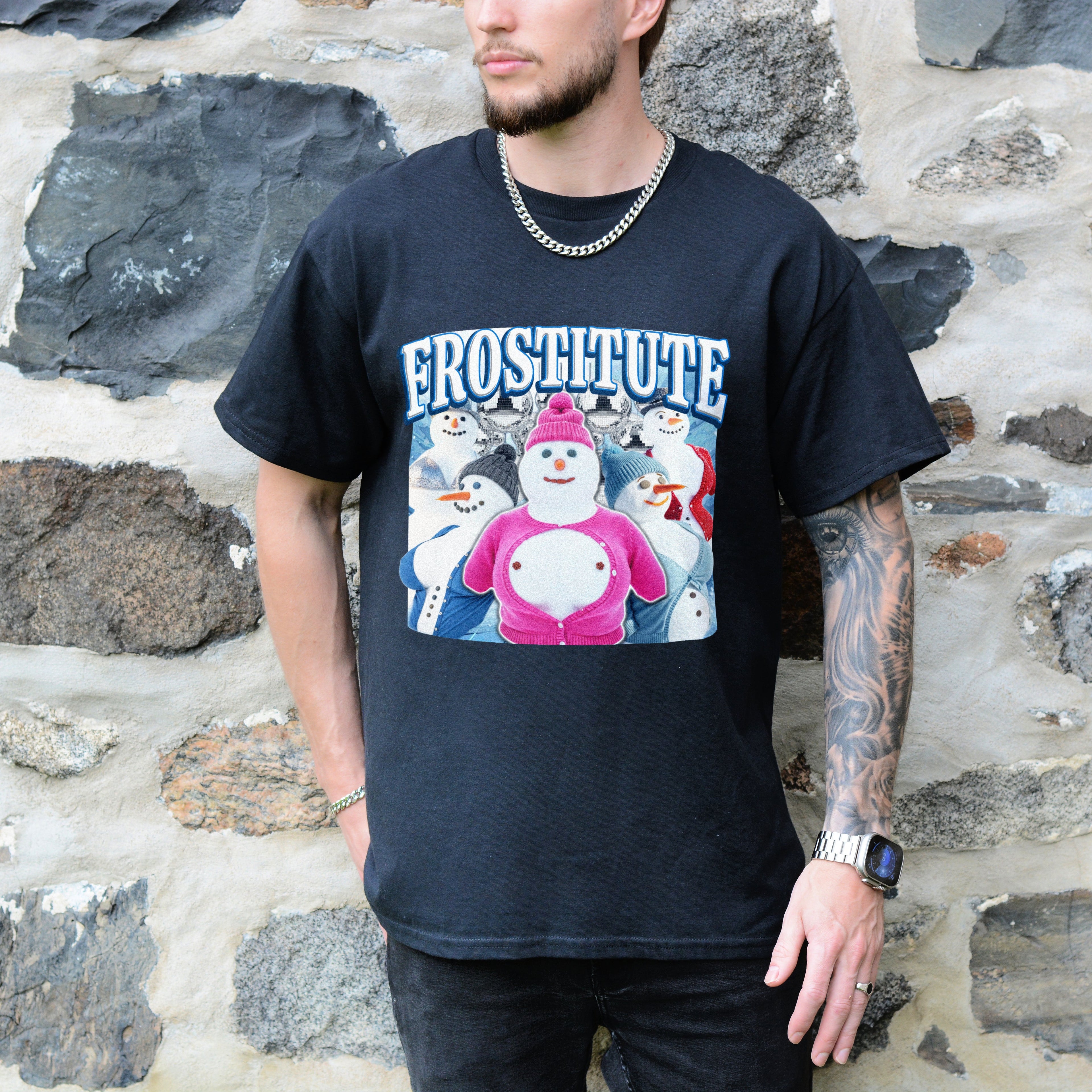 Person wearing a black t-shirt with a graphic design of snowmen and text, standing against a stone wall.