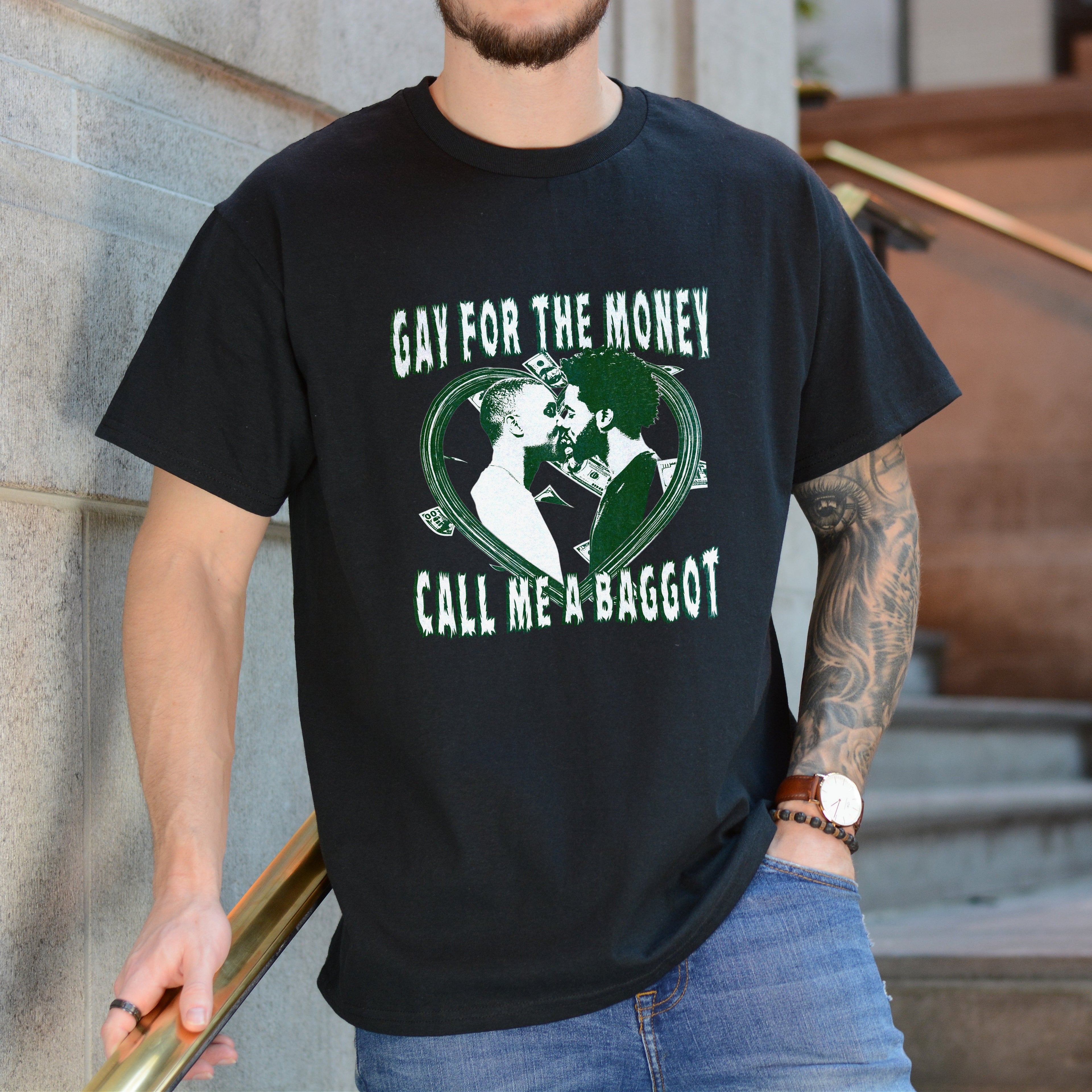 Person wearing a black t-shirt with graphic design and text, standing against a building.