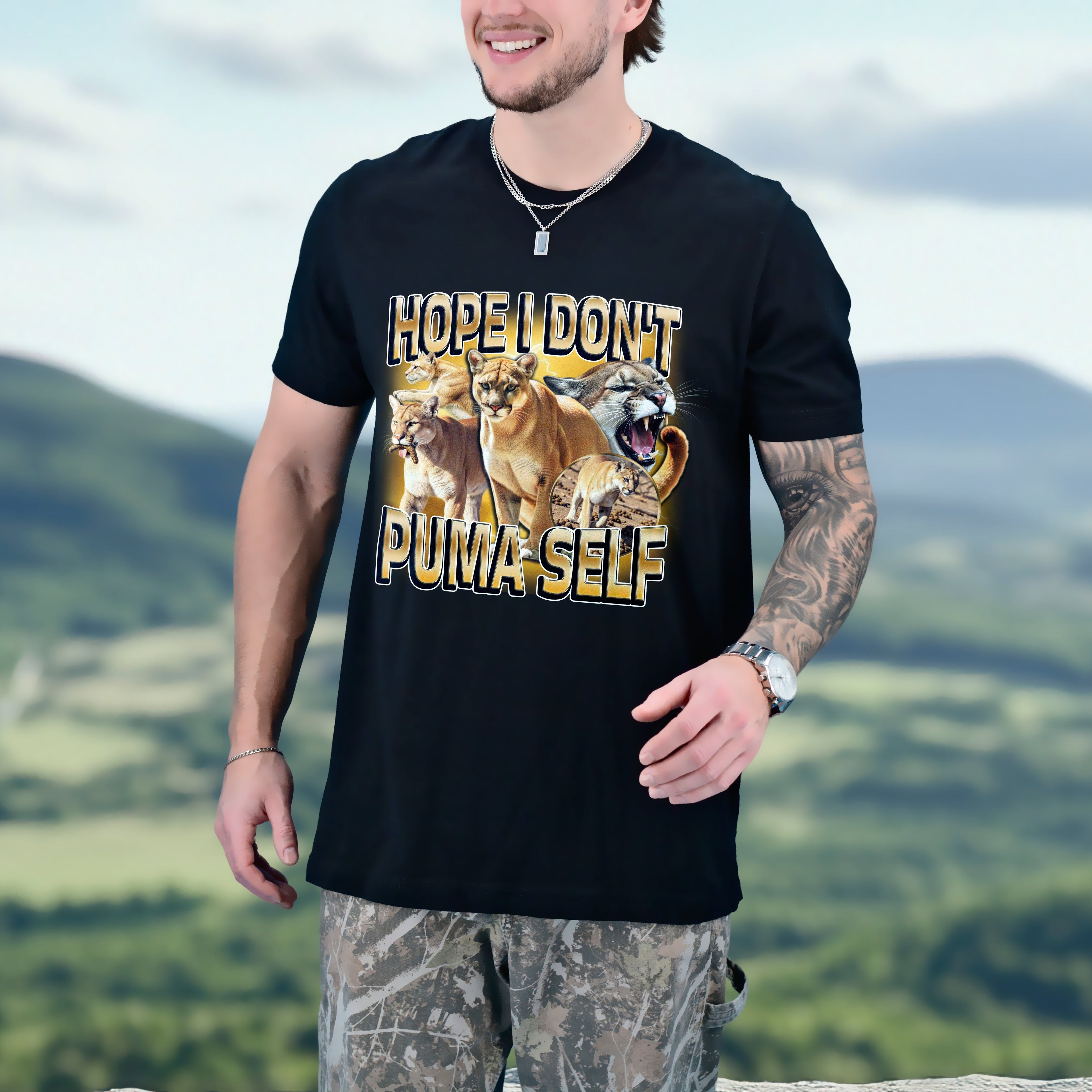 Man wearing a black t-shirt with a graphic design and text, standing outdoors with mountains in the background.