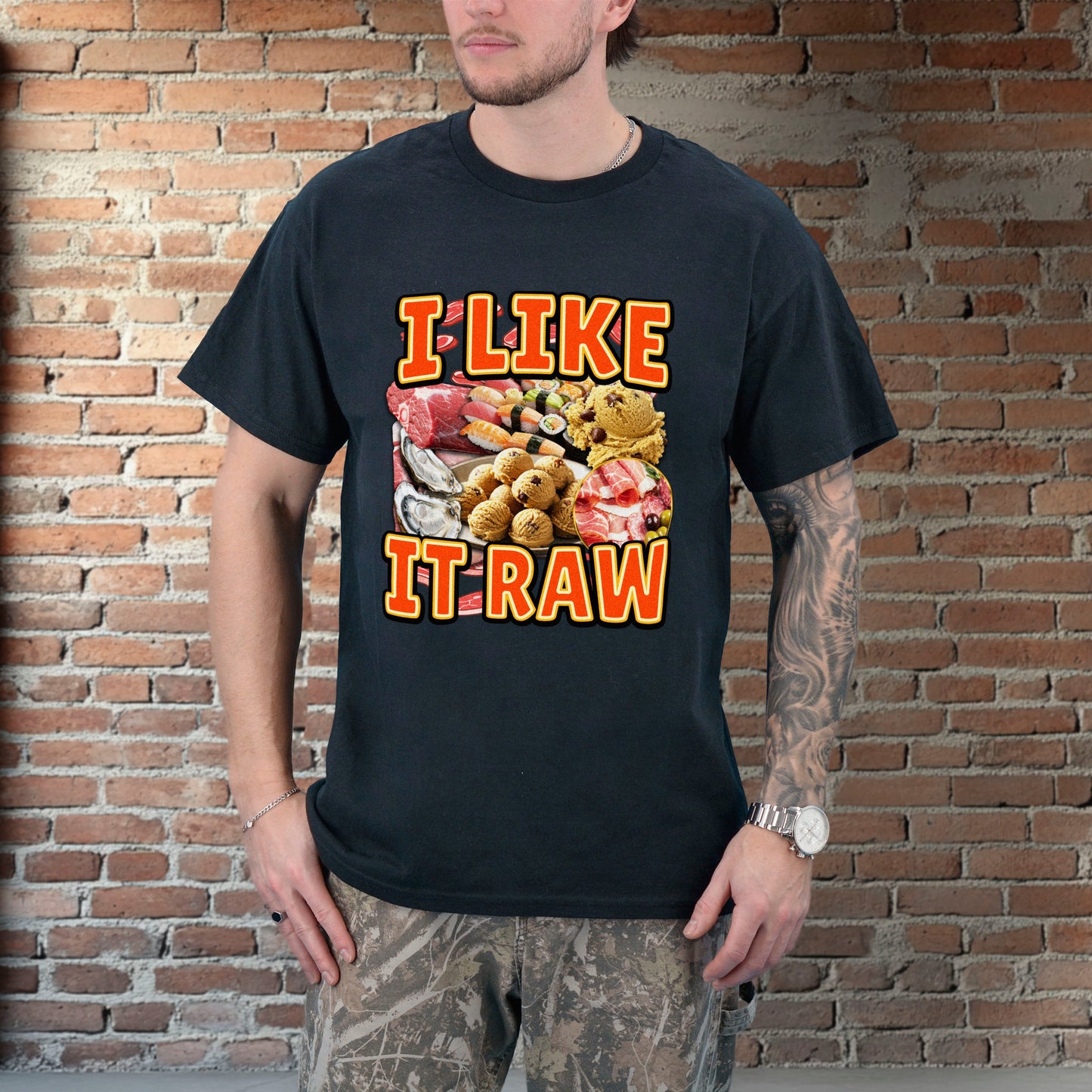 Person wearing a black t-shirt with 'I LIKE IT RAW' graphic design against a brick wall.