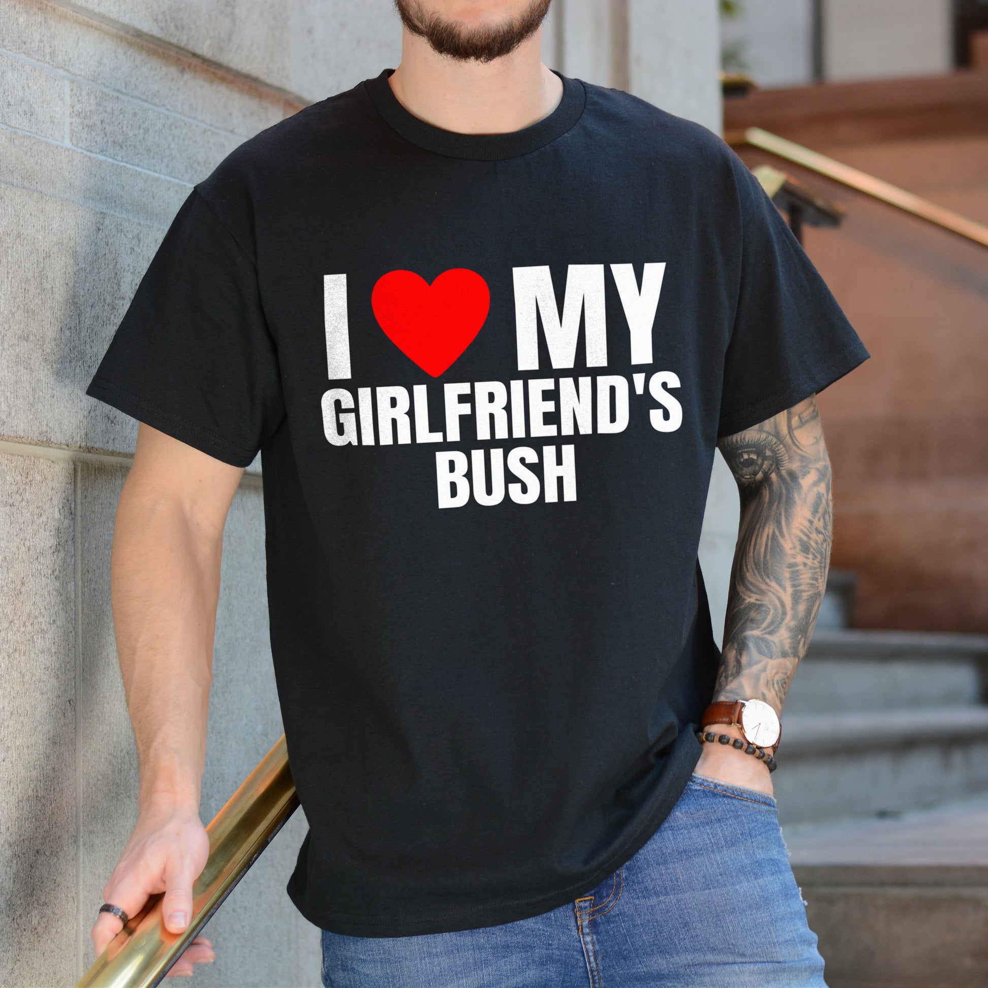 Person wearing a black t-shirt with humorous text design, standing against a building.